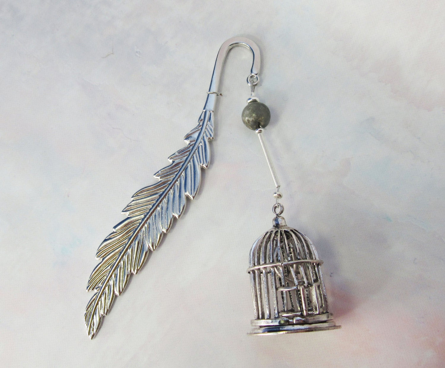 BIRD CAGE BOOKMARK - Feather Metal Bookmarker elegantly displayed with a book, highlighting its unique trinket design for avid readers.