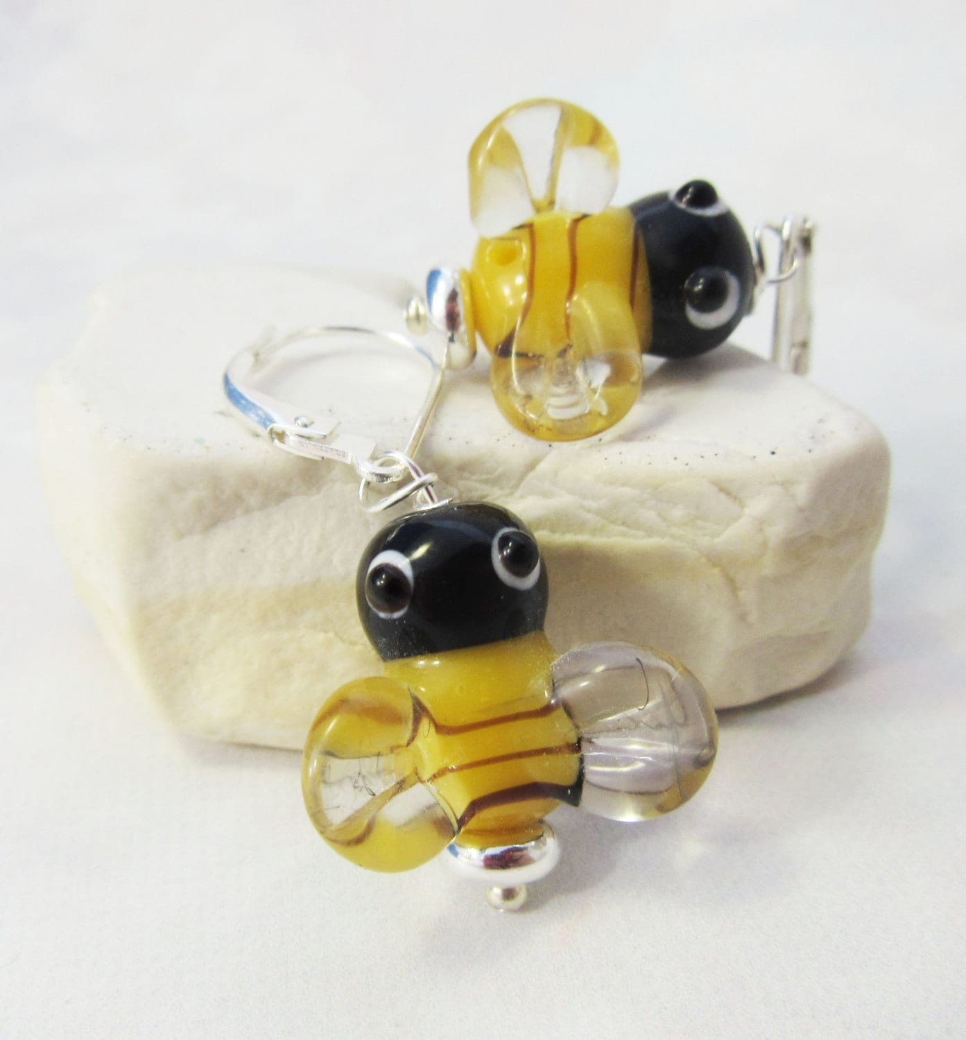 Handcrafted Honey Bee Art Glass Earrings feature yellow, black, and clear bee-shaped charms on sterling silver lever backs, displayed on a light stone background.