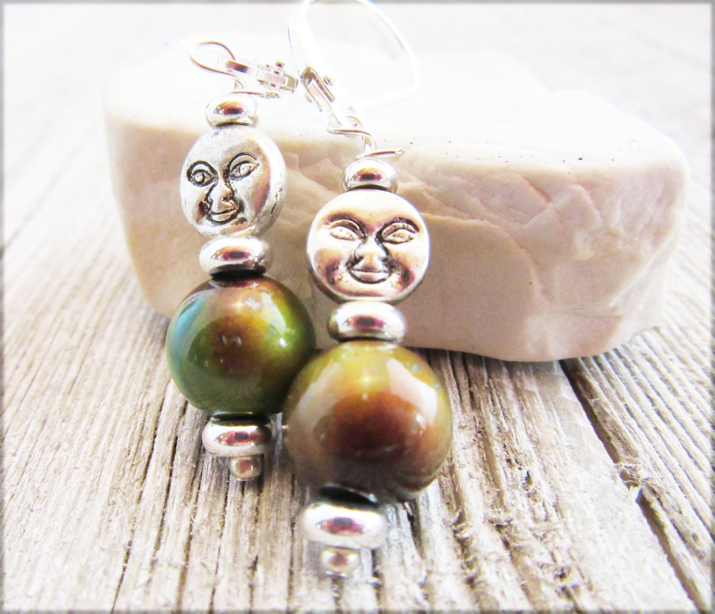 Spring Full Moon Silver Earrings with Color Changing Mood Beads showcase a lunar crescent moon face design and large green-brown mood beads, displayed on light wood with a white stone in the background.