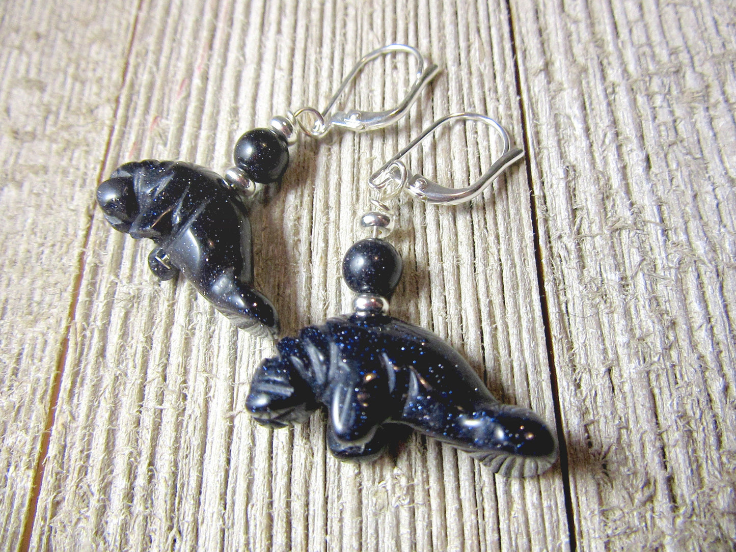 Deep Blue or Goldstone Manatee Earrings: artisan-designed sea life jewelry featuring dark blue sparkly goldstone beads and silver hooks, perfect as a gift for sea life lovers, displayed on a wood-textured surface.