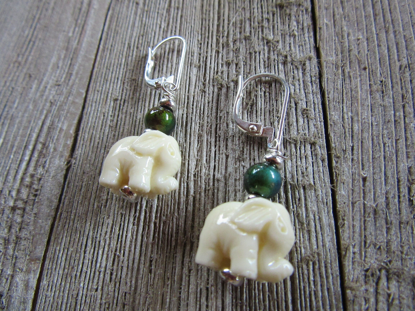Elephant Earrings – Boho Mood Beads feature cream elephant charms and a sterling silver color change topper bead, displayed on rustic wood. Only one pair available.