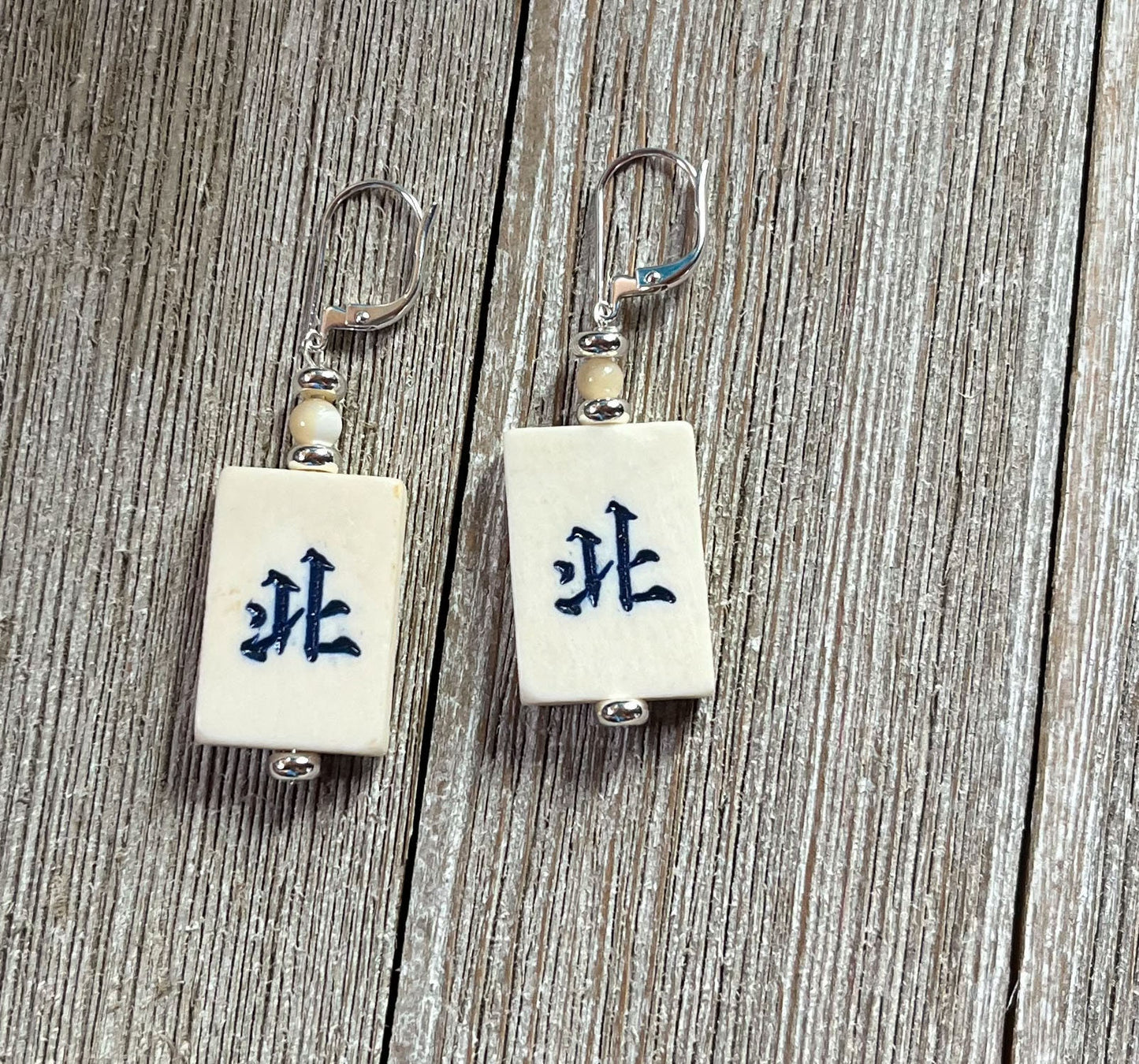 Mahjong Tile Earrings: Green Dragon Jewelry feature white rectangular tiles with green Chinese characters, metal hooks, and beige beads—displayed on rustic wood. A unique gift for any Mahjong player.