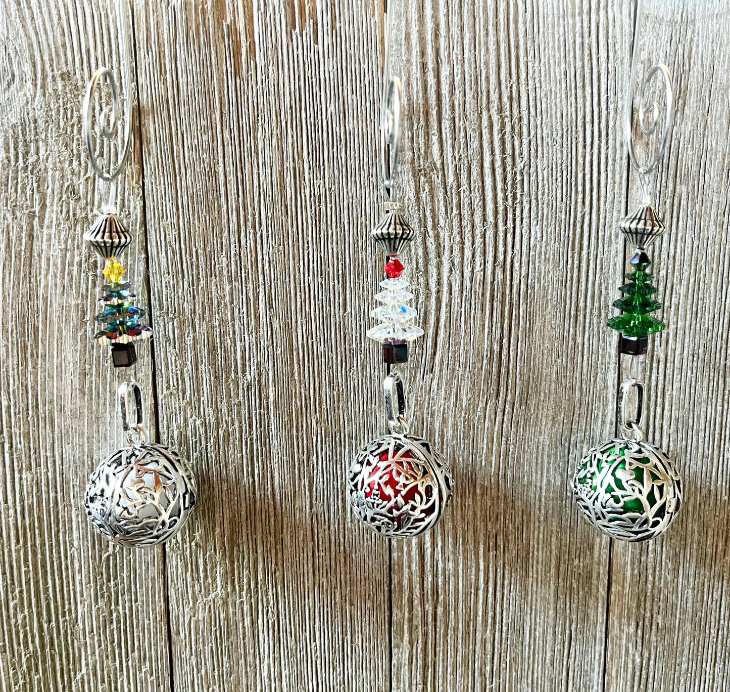 Three Crystal Christmas Tree Ornament - Scent Locket Holiday Decorations hang against a wood backdrop, each featuring a beaded Christmas tree in yellow, red, or green above an ornate silver sphere.
