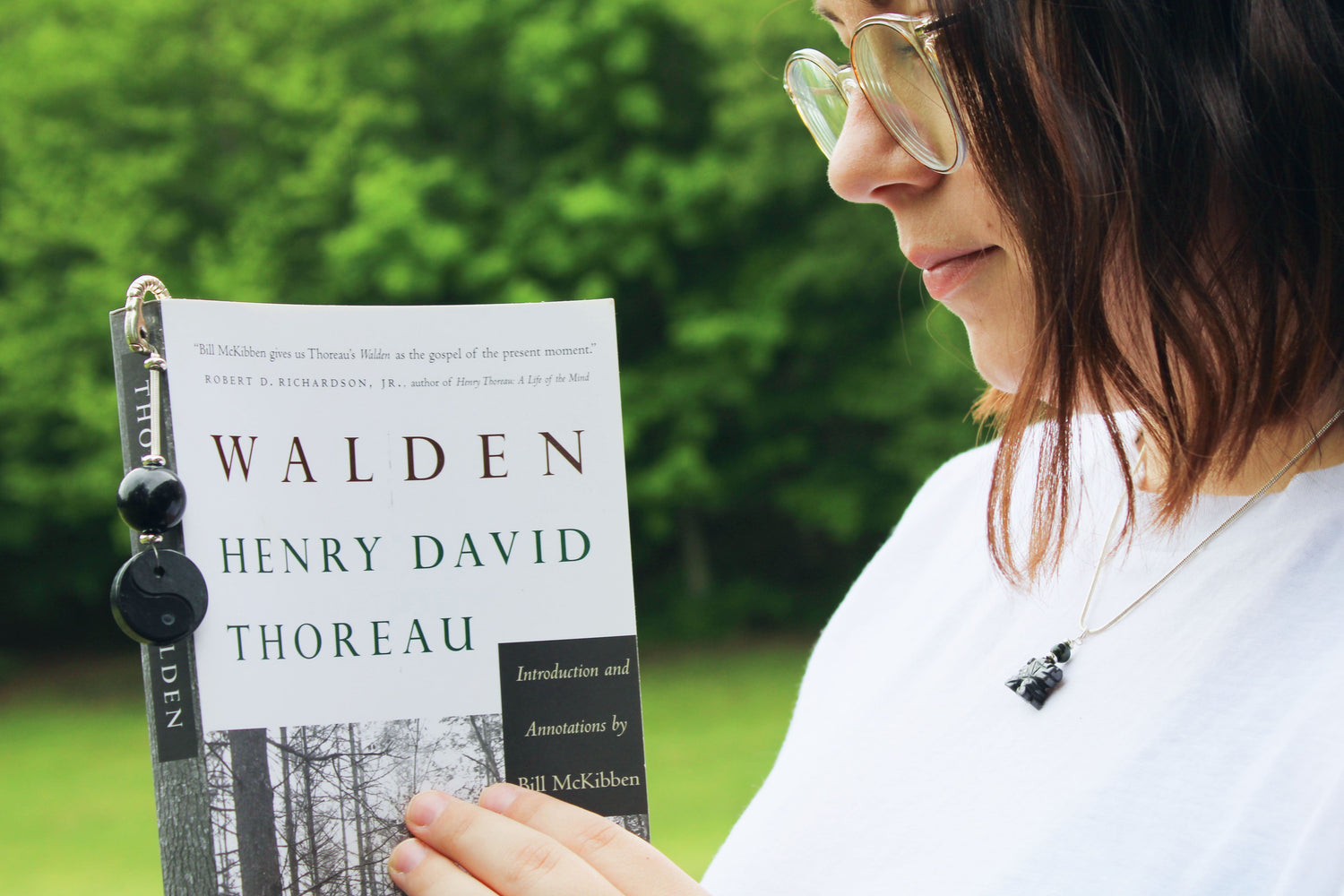 Woman holding the book 'Walden' by Henry David Thoreau, wearing a stylish aromatherapy necklace featuring an essential oil locket from the Newest Designs collection, perfect for enhancing creativity and self-expression.