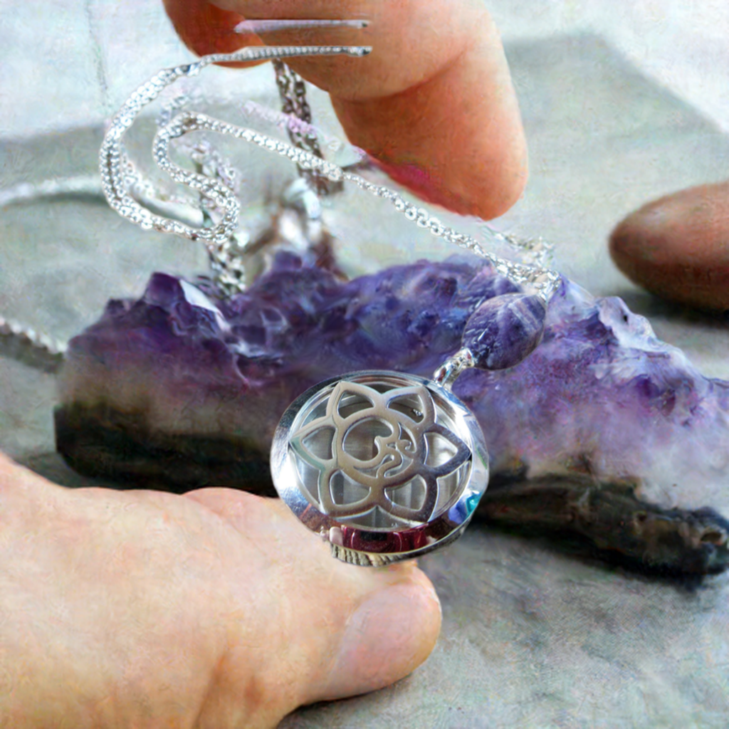 Aromatherapy necklace with intricate flower design being held above a healing amethyst crystal, showcasing the blend of beauty and functionality in essential oil jewelry.