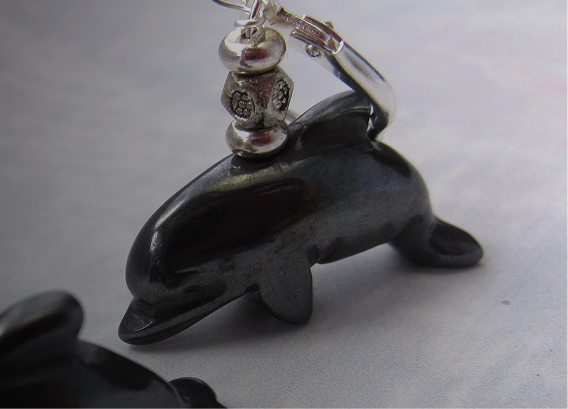 A close-up of a dolphin-shaped black pendant with silver beads and a ring attached on top, placed on a light surface.