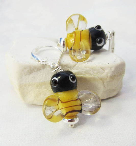Handcrafted Honey Bee Art Glass Earrings feature yellow, black, and clear bee-shaped charms on sterling silver lever backs, displayed on a light stone background.