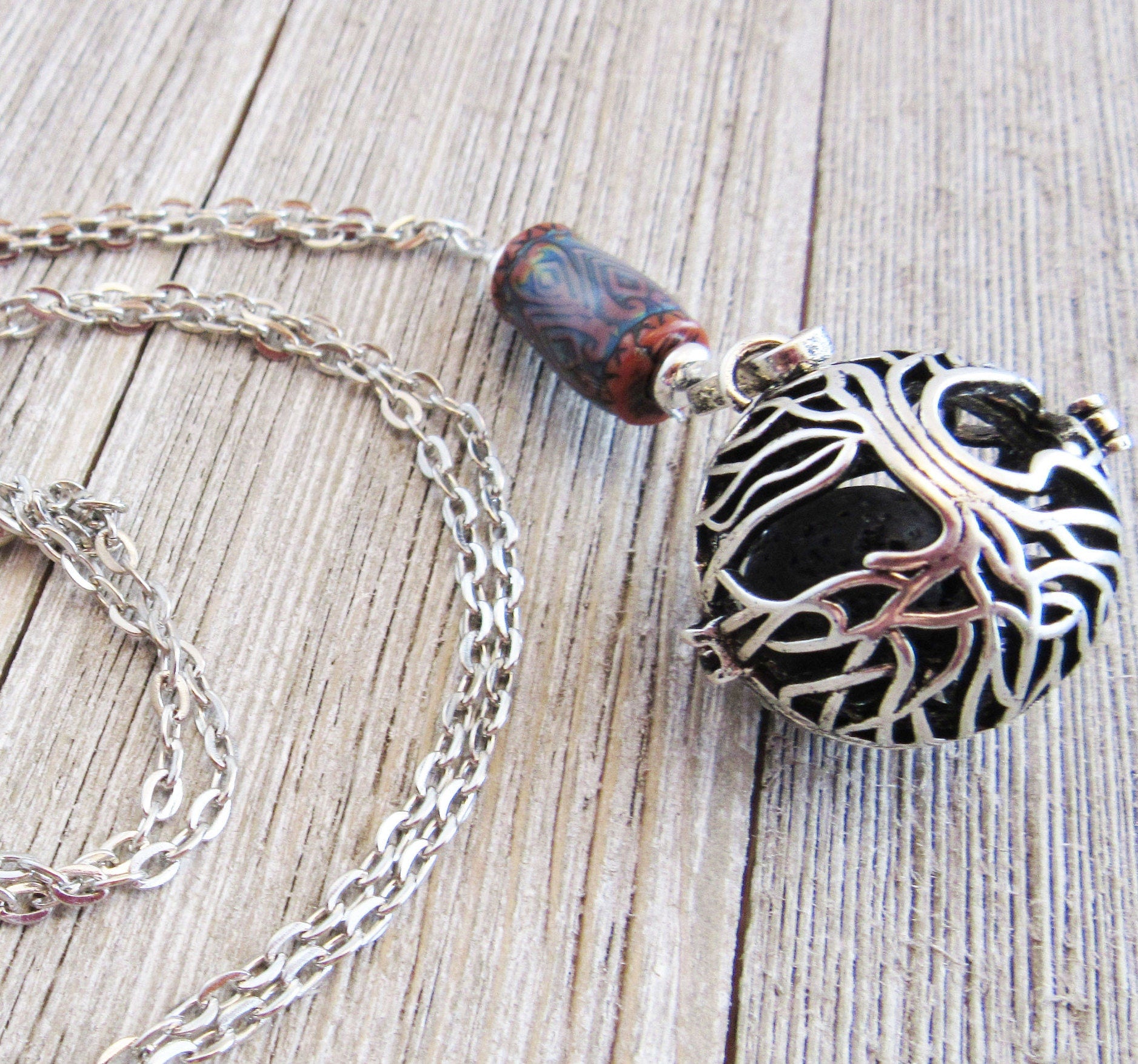 The Tree of Life Essential Oil Diffuser Necklace features a color-changing gemstone and artisan design, with an intricate tree overlay pendant, displayed on a weathered wooden surface.