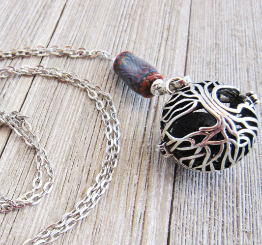 The Tree of Life Essential Oil Diffuser Necklace features a color-changing gemstone and artisan design, with an intricate tree overlay pendant, displayed on a weathered wooden surface.