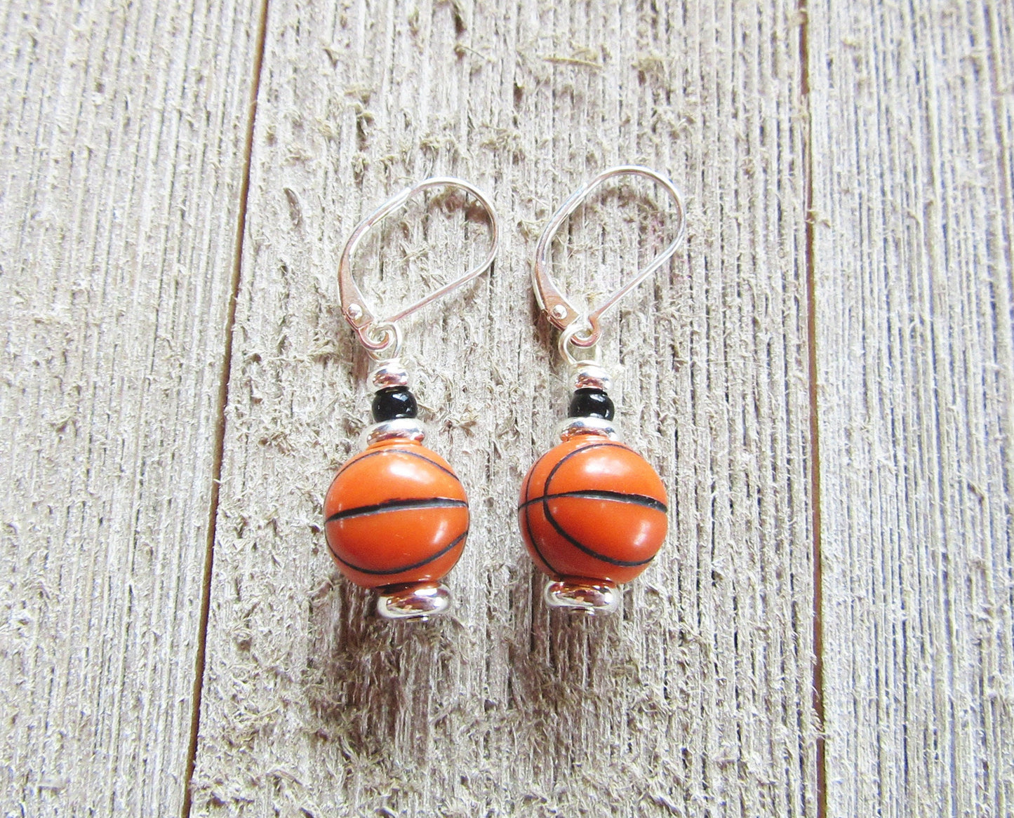 Hand-crafted Basketball Earrings—sports jewelry with small basketball-shaped beads and sterling silver lever backs—displayed on a rustic wooden surface.