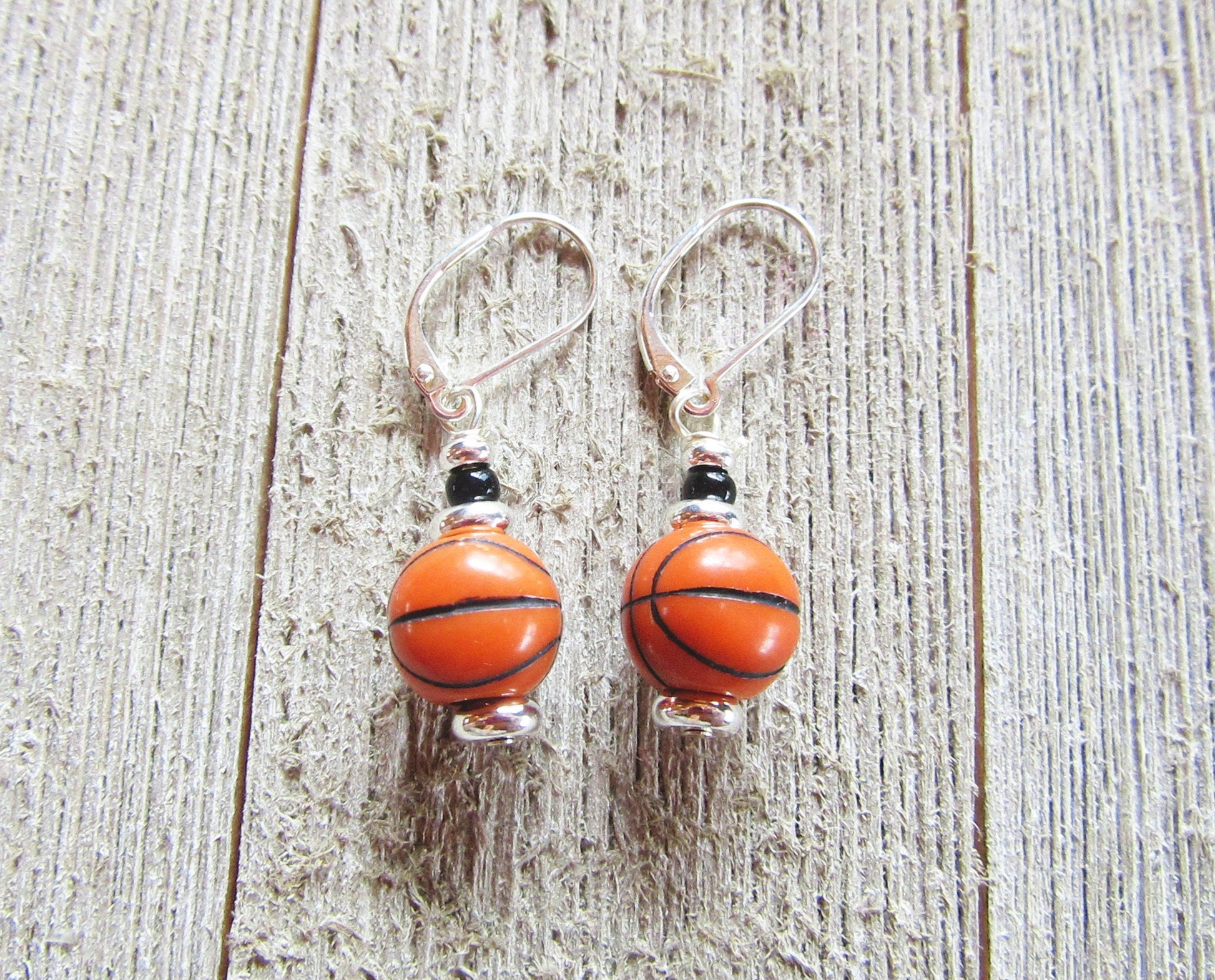 Hand-crafted Basketball Earrings—sports jewelry with small basketball-shaped beads and sterling silver lever backs—displayed on a rustic wooden surface.