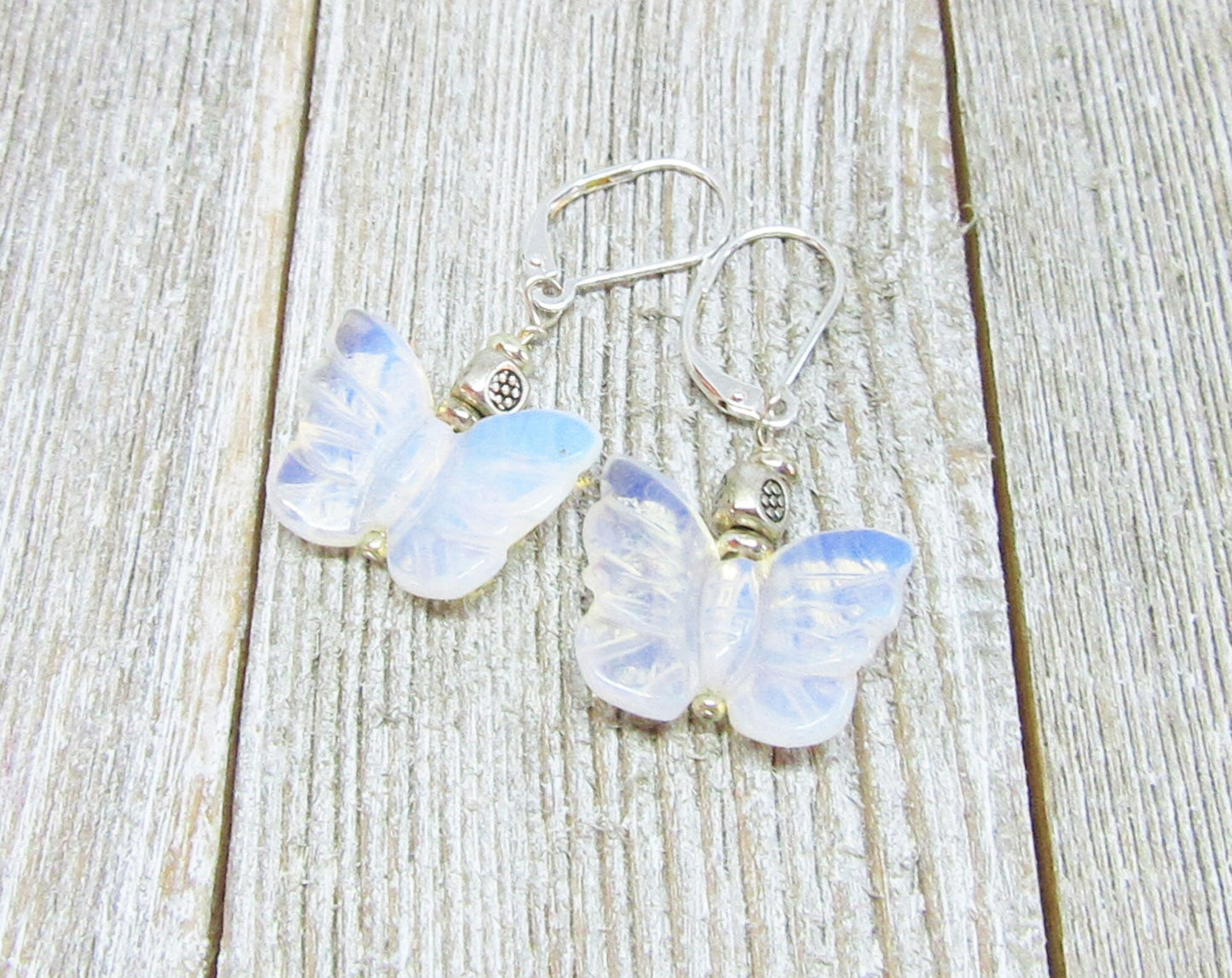 Handcrafted Rose Quartz Butterfly Earrings with sterling silver lever backs are elegantly displayed on a weathered wooden surface, showcasing butterfly-shaped rose quartz pendants and quality silver craftsmanship.