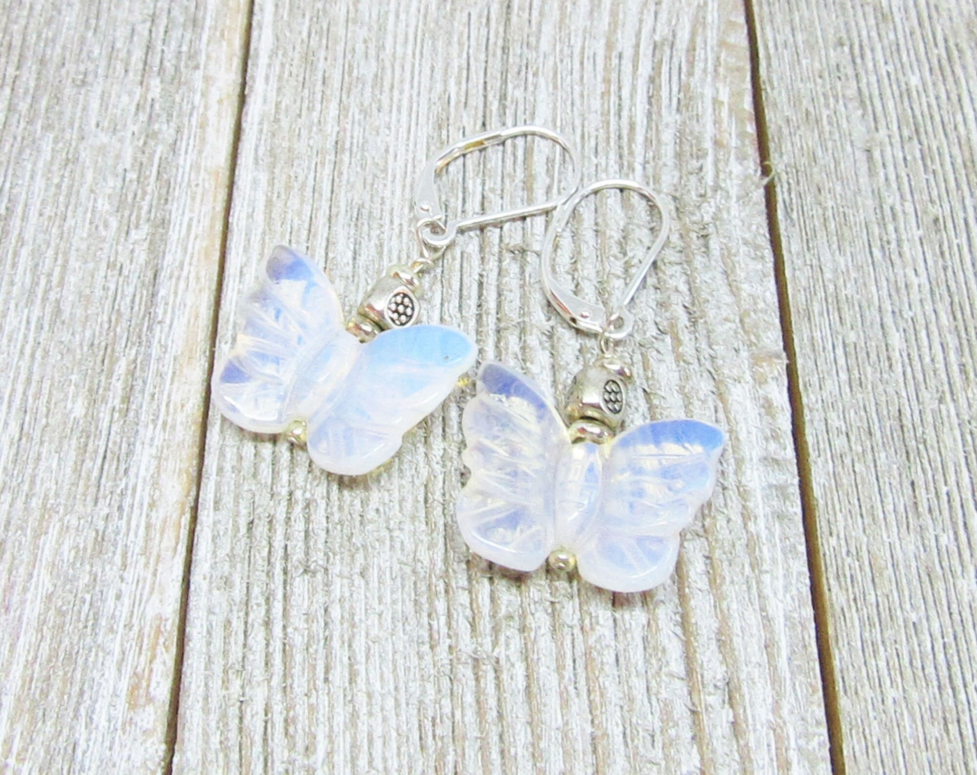 Handcrafted Rose Quartz Butterfly Earrings with sterling silver lever backs are elegantly displayed on a weathered wooden surface, showcasing butterfly-shaped rose quartz pendants and quality silver craftsmanship.