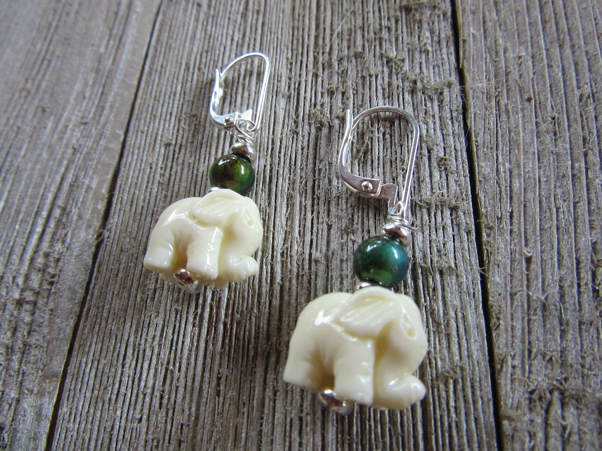 Elephant Earrings – Boho Mood Beads feature cream elephant charms and a sterling silver color change topper bead, displayed on rustic wood. Only one pair available.