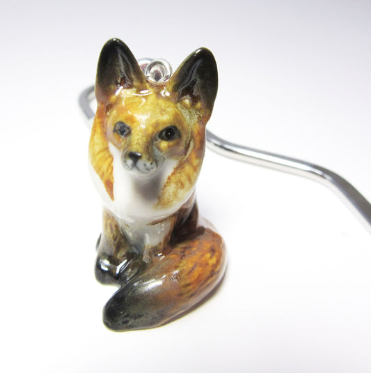 A Handmade Painted Fox Bookmark—a small, glossy ceramic fox with a curled tail—is perched on a white surface, its silver metal hook partly visible. This unique reading accessory makes an ideal gift for book lovers.