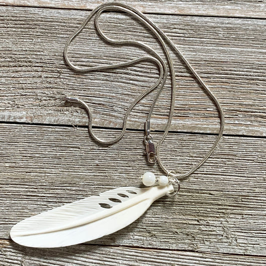 The White Feather Necklace features an angel sign carved bone and mother of pearl pendant, displayed on a rustic wooden surface—ideal for those seeking meaningful spiritual jewelry.