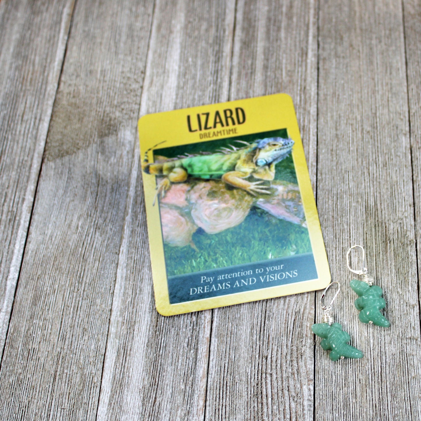A lizard-themed oracle card sits on wood beside Handcarved Aventurine Lizard Earrings: Herpetologist Gift. Perfect lizard jewelry, the card reads: “Lizard—Dreamtime. Pay attention to your dreams and visions.”.