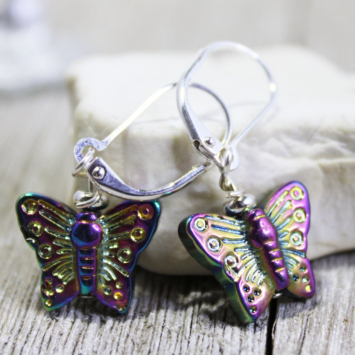 Shimmery Butterfly Earrings: AB Crystal Aurora Borealis Finish, with metallic purple, green, and gold butterfly accents on sterling silver lever-back hooks, displayed against a soft neutral background.