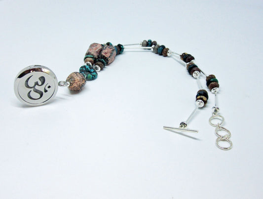 A beaded bracelet with mixed stones and silver accents plus a round charm engraved with the Om symbol, ideal for pairing with your Rhodochrosite Turquoise Essential Oil Diffuser Necklace or Silver Namaste Locket. Shown on a white background.