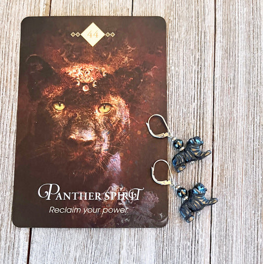 A card showing a black panther, "Panther Spirit," "Reclaim your power," and the number 44 rests on wood beside Enchanting Panther Hematite Earrings—unique animal jewelry perfect for big cat lovers with grounding blue accents.