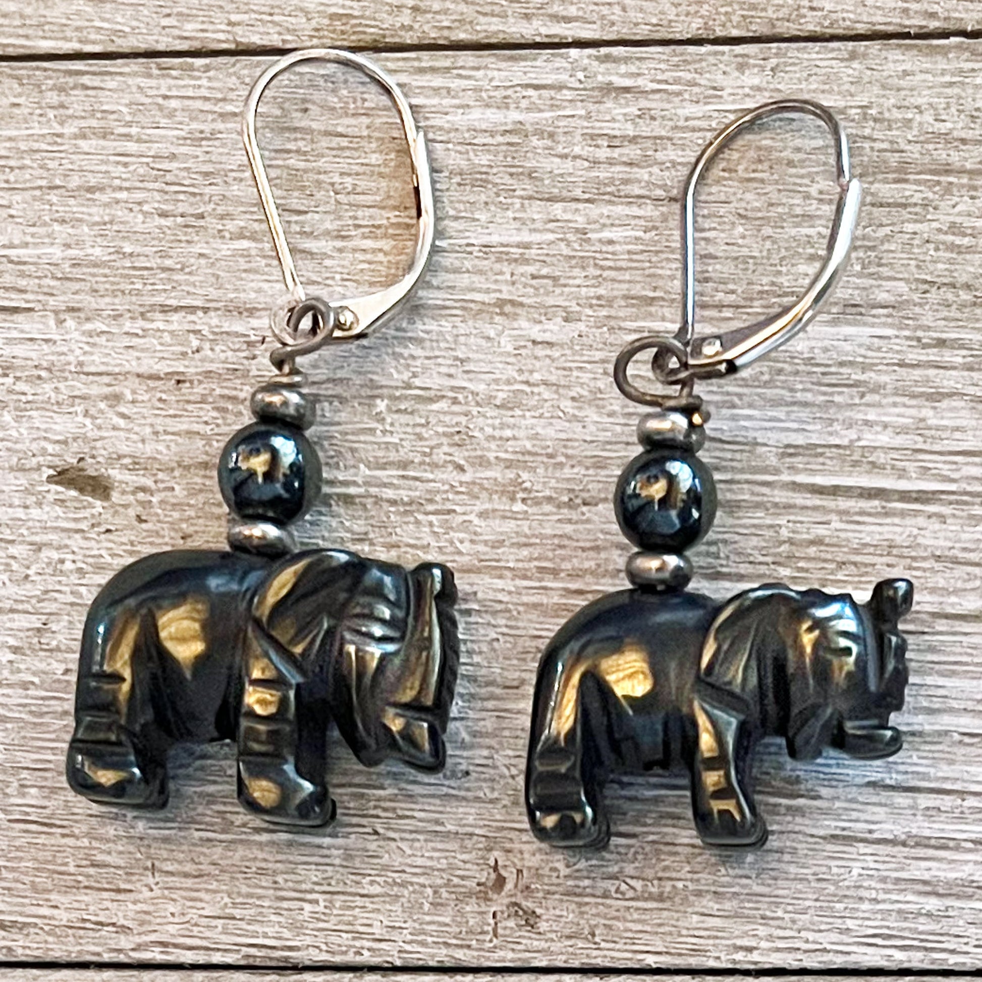 A pair of Elephant Earrings: Sterling Silver Dangle Lever Backs, featuring small elephant-shaped charms with round black beads, displayed on a light wooden surface. Multiple stones available.