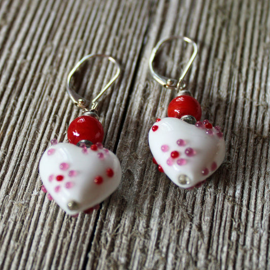A pair of Lampwork Glass Heart Dangle Earrings—red and white lever back jewelry with heart-shaped beads—displayed on a wooden surface.