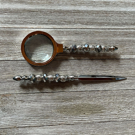The Handmade Silver Desk Set features a magnifying glass and letter opener with faceted bead handles, shown here lying on a wooden surface.
