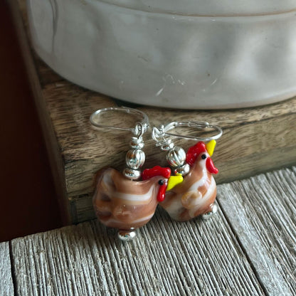 Close-up view of the unique white lamp work glass hen earrings - perfect gift for barnyard keepers.