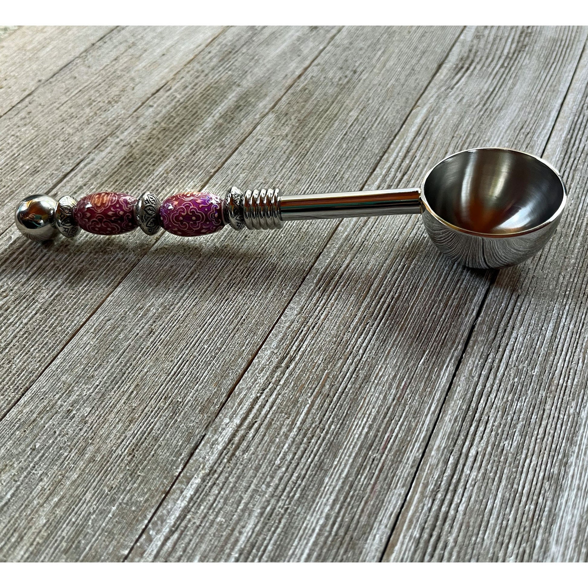 The Color-Changing Beaded Scoop: Herb, Bath Salt, Coffee Spoon—with purple and silver accents and an ornate handle—rests on a rustic wooden surface, making it a unique astrology gift or spiritual ritual tool.