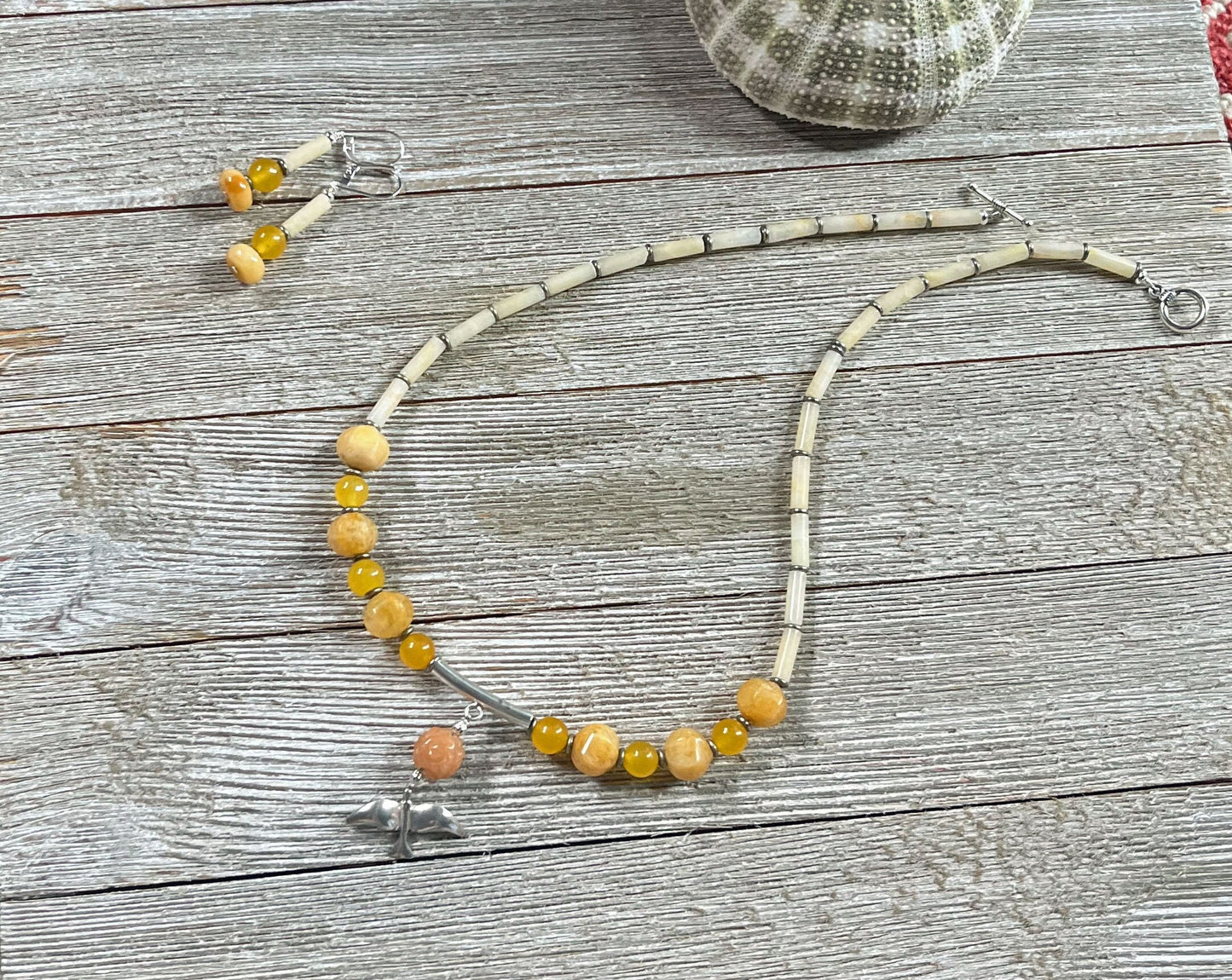 The Sterling Silver Bird Aventurine Necklace Earrings Set from Zen Artisan Jewelry is displayed on a wooden surface with matching earrings, a sea urchin shell, and other artisan pieces.