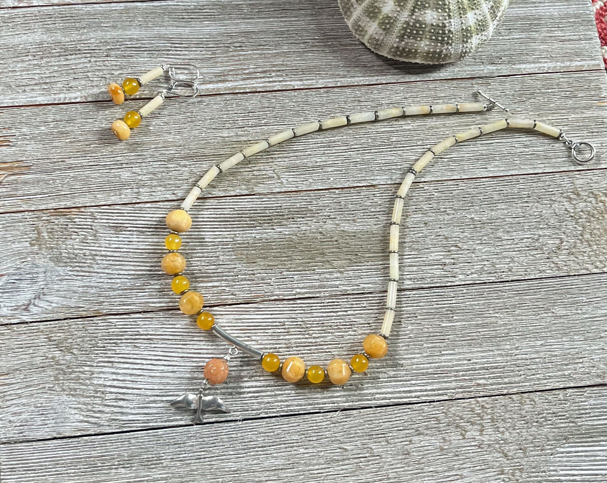 The Sterling Silver Bird Aventurine Necklace Earrings Set from Zen Artisan Jewelry is displayed on a wooden surface with matching earrings, a sea urchin shell, and other artisan pieces.