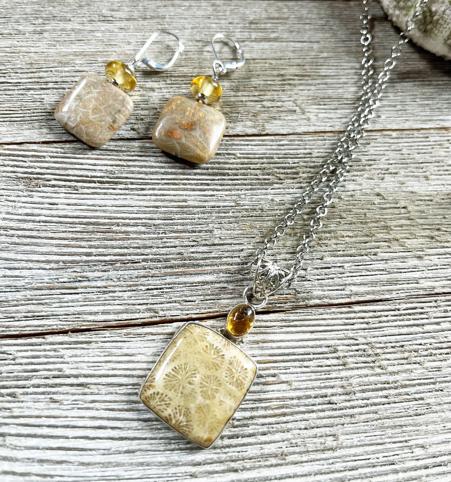 The Fossil Coral Jewelry Set features a 24" necklace with square beige fossil stone pendants, amber beads, and matching topaz sterling silver earrings, beautifully displayed on rustic wooden boards.