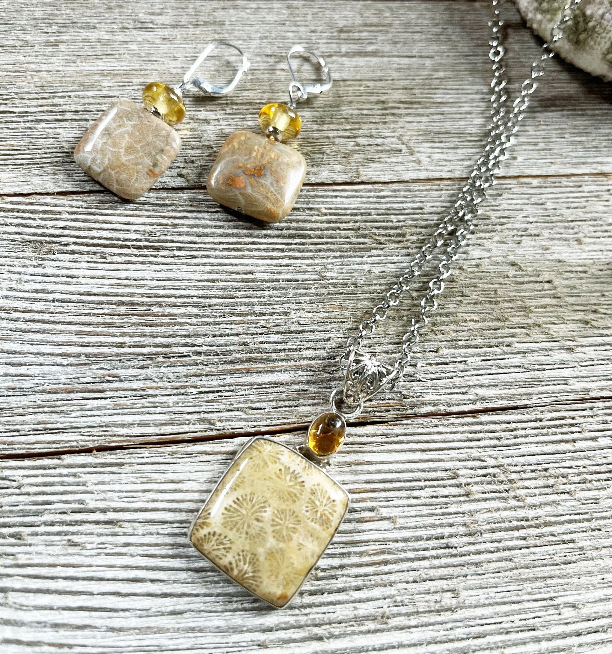 The Fossil Coral Jewelry Set features a 24" necklace with square beige fossil stone pendants, amber beads, and matching topaz sterling silver earrings, beautifully displayed on rustic wooden boards.