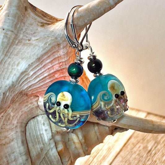 Lamp-worked Glass Octopus Earrings: Handcrafted Mood Bead Jewelry featuring blue beads with yellow octopus designs, set against a shell backdrop with a wooden surface.