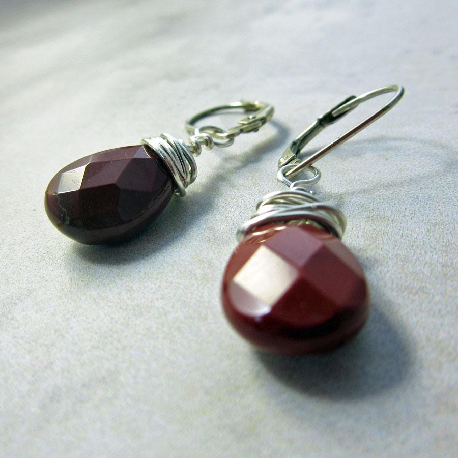 Moukite Briolette Earrings feature faceted, teardrop-shaped dark red gemstones wire-wrapped and displayed on a light grey surface, completed with secure sterling silver lever-back hooks.