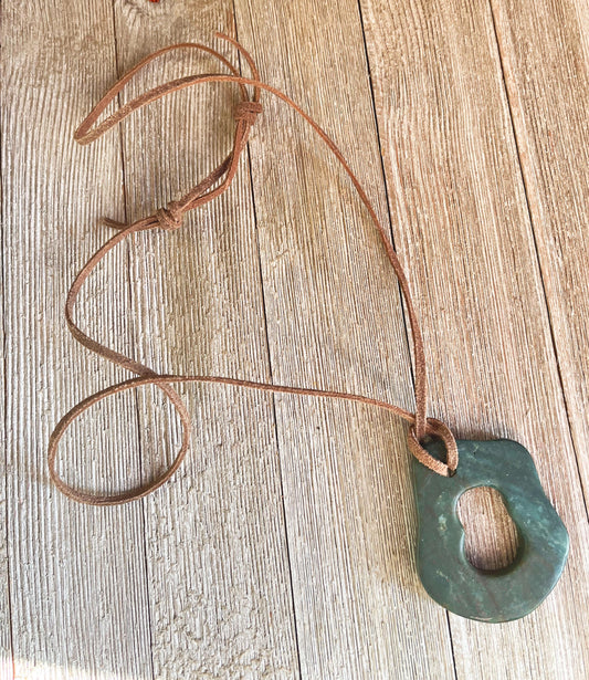 The Handcrafted Green Aventurine Pendant Necklace features an irregular greenstone pendant with a central hole on an adjustable leather cord, displayed on a light wooden surface.