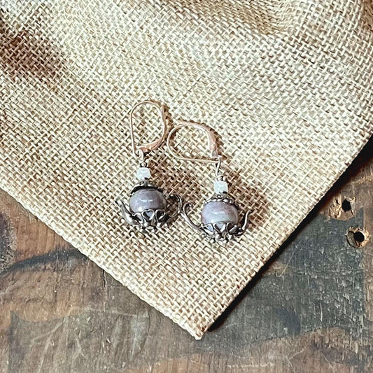Sterling Silver Teapot Earrings feature round lavender jasper stones and whimsical design, displayed on burlap fabric over a wooden surface.