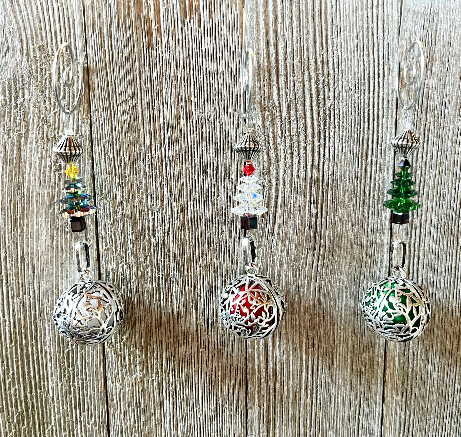 Three Crystal Christmas Tree Ornament - Scent Locket Holiday Decorations hang against a wood backdrop, each featuring a beaded Christmas tree in yellow, red, or green above an ornate silver sphere.