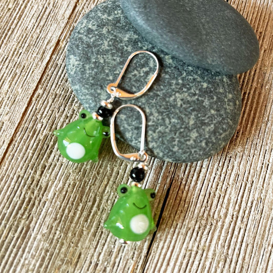 Handcrafted Glass Frog Earrings: Animal Lover Jewelry Gift featuring silver hooks and frog charms, elegantly displayed on stacked gray stones atop rustic wood—a delightful accessory for any animal jewelry enthusiast.