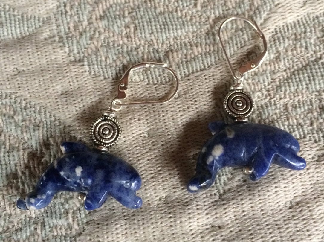 Handmade Sodalite Dolphin Earrings feature blue sodalite dolphin charms with white speckles, silver bead accents, and sterling silver lever-back hooks, displayed on a textured fabric background.