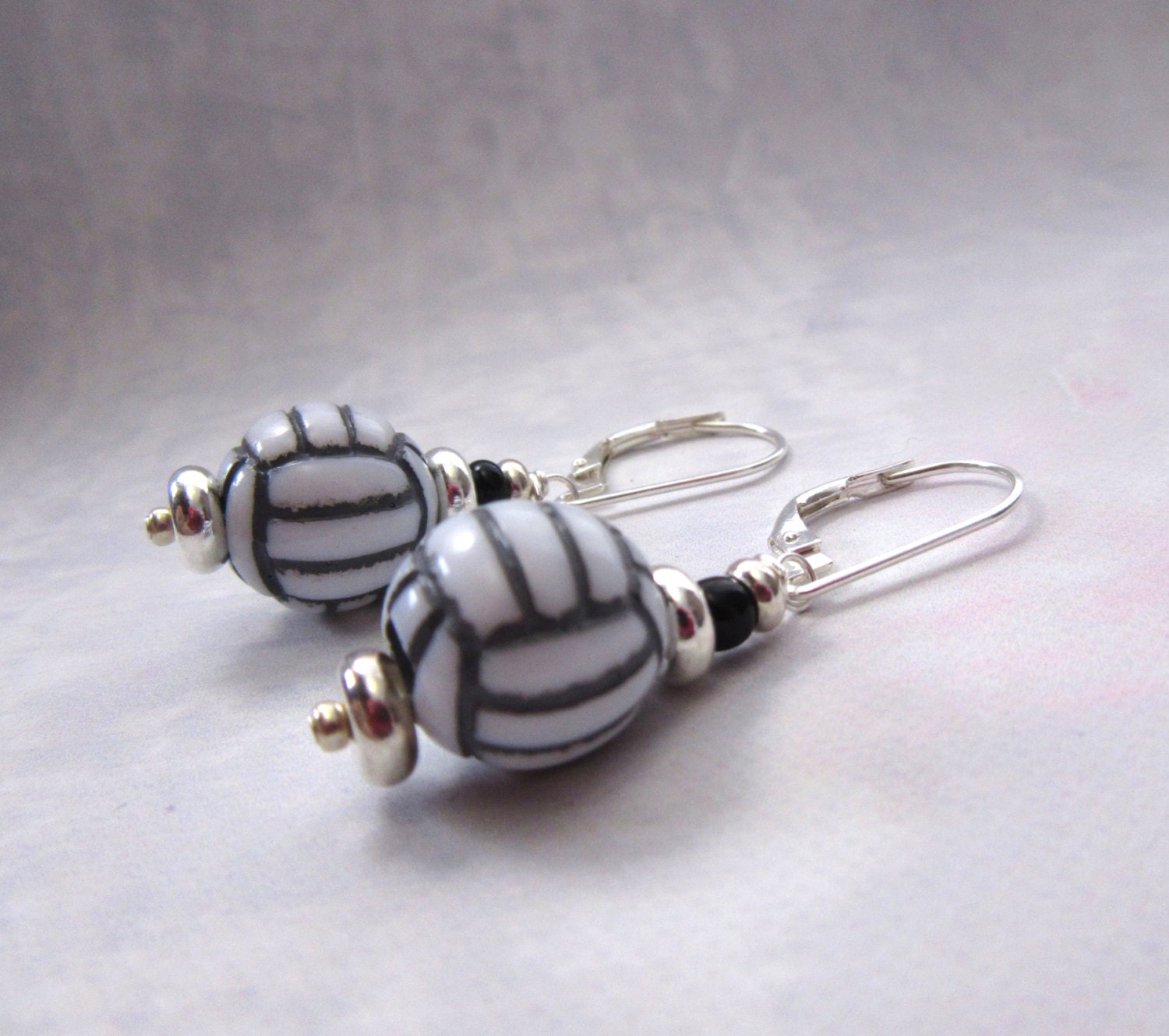 Handmade Volleyball Earrings featuring oval beads with black and white stripes, sterling silver lever backs, and sporty style—perfect for fans of unique sport jewelry. Displayed on a light background.
