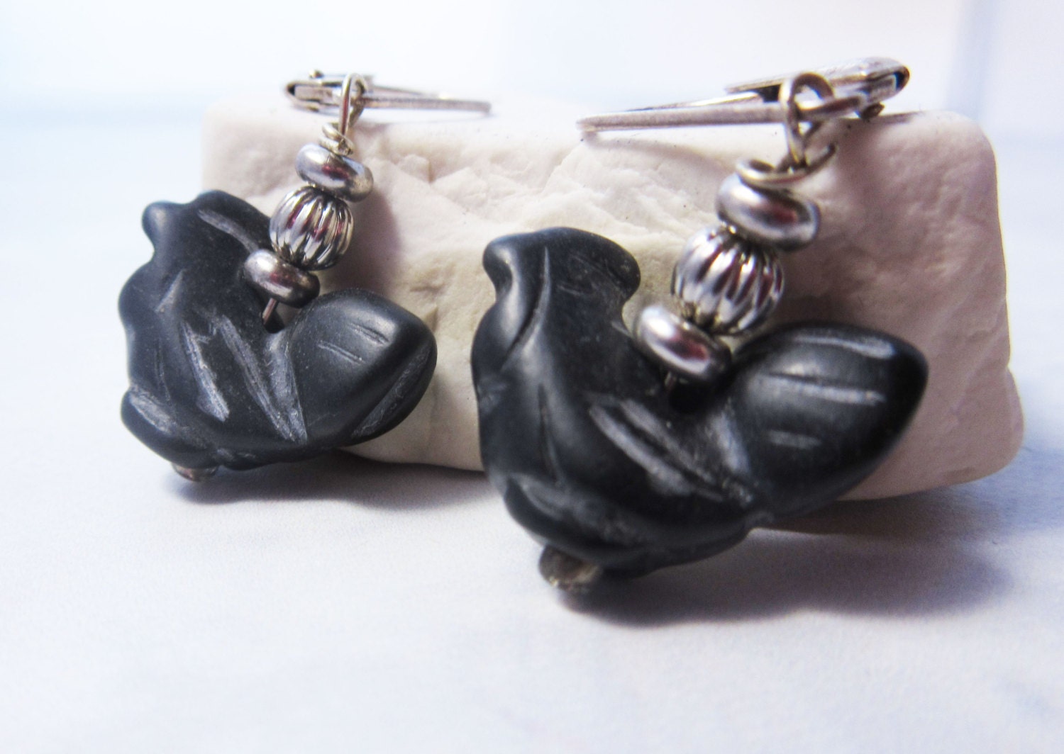Hand-Carved Obsidian Rooster Earrings feature black rooster-shaped beads with silver round spacers, shown on a white stone background—ideal for anyone who loves unique farm animal jewelry.