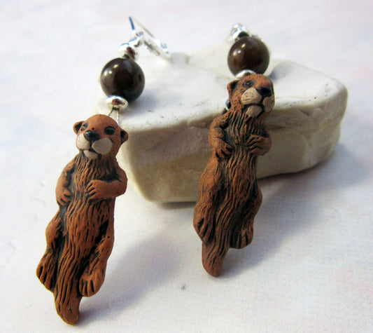 Hand Painted Sea Otter Earrings with abalone topper beads and sterling silver, showcasing detailed otter charms on a light-colored stone background.