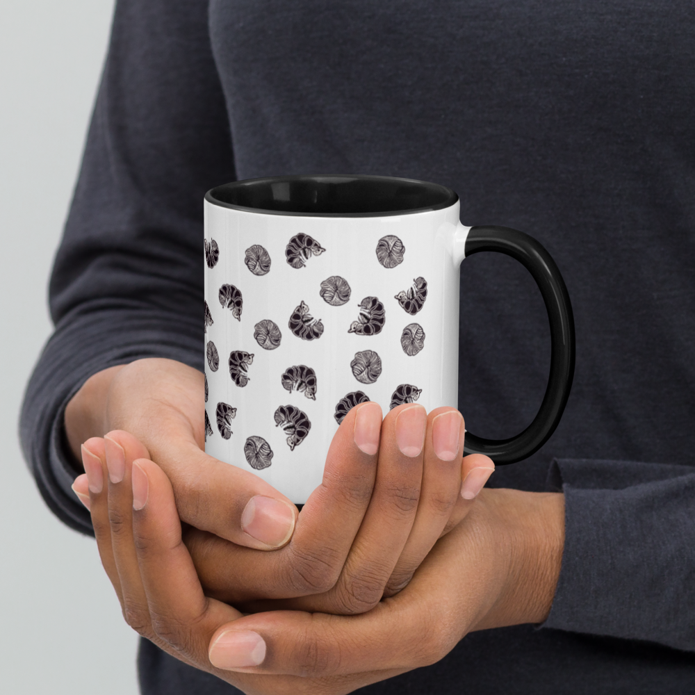 A person in a dark long-sleeve shirt holds Enlivenadorn by Gwynstone’s Roly Poly Pill Bug Isopod Mug with Color Inside, a white mug with a black handle adorned with charming pill bug illustrations—ideal for any isopod or arthropod enthusiast.